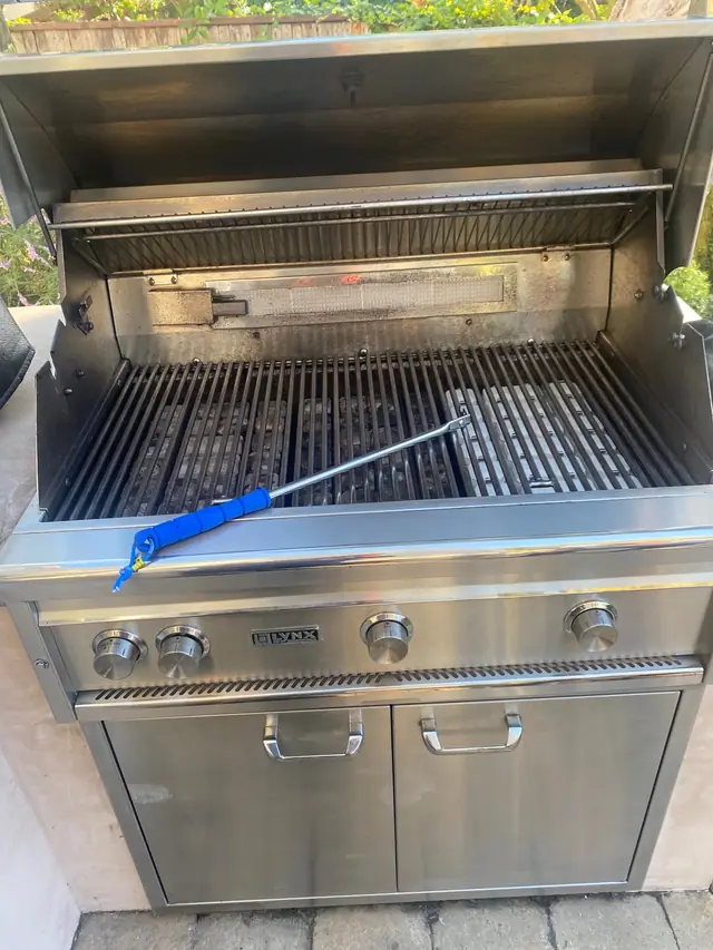 A blue grill brush resting across clean stainless grates under an open hood