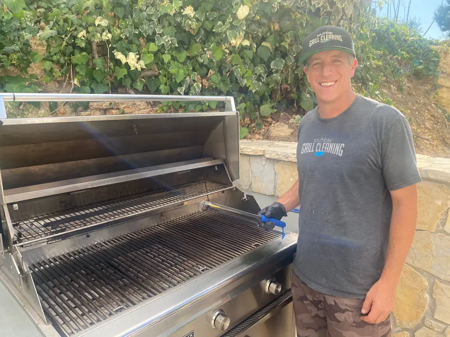 A South Bay Grill Cleaning crew member in a branded shirt and cap beside a clean grill, holding a brush